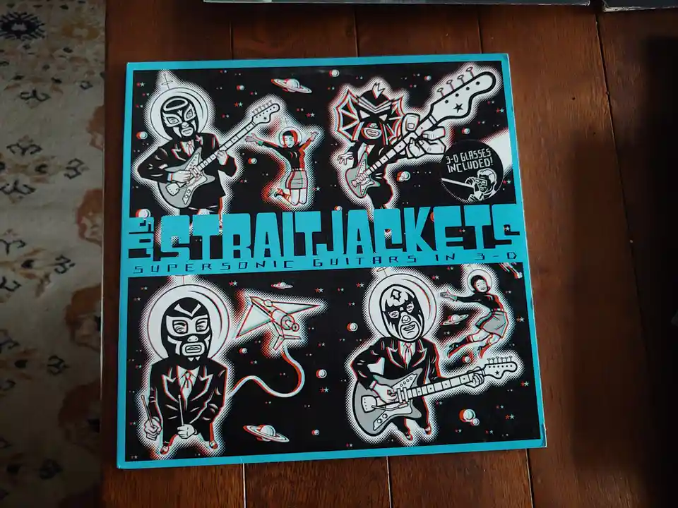 A vintage-style album cover for 'The Straitjackets' titled 'Supersonic Guitars in 3-D' features cartoonish figures in space…