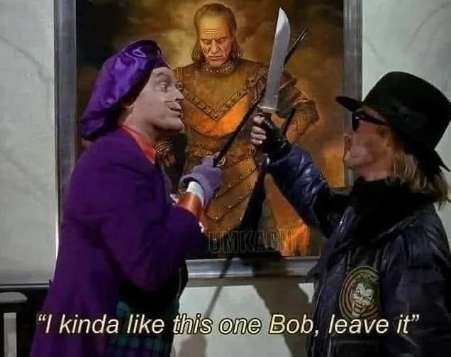 Two men stand before a framed portrait of a stern-looking armored man. The man on the left, wearing a purple outfit and hat…