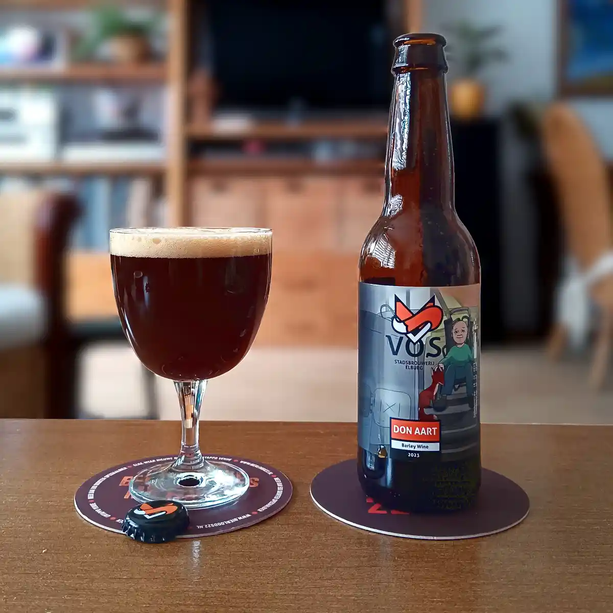 A dark beer bottle labeled 'DON AART Barley Wine 2023' from 'VOS STADSBRUWERIJ ELBURG' sits next to a filled glass on…