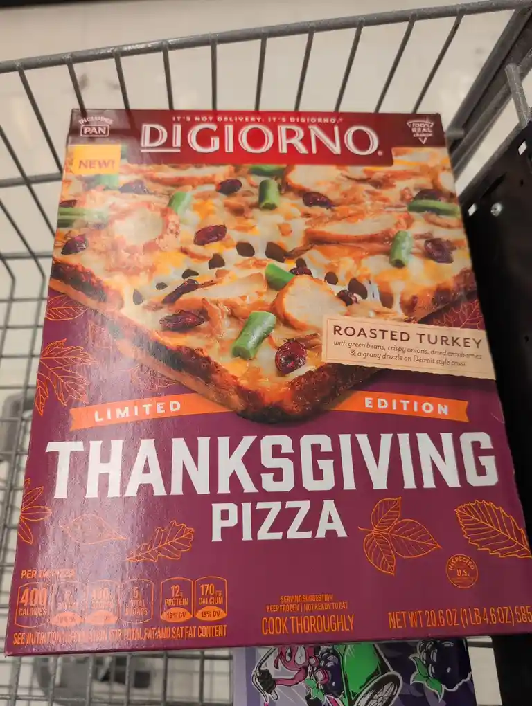 A Digiorno Thanksgiving pizza box, labeled 'Limited Edition', sits in a shopping cart. The box features an image of a pizza…