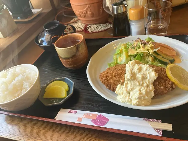 a close-up photo of a Japanese katsu meal served on a black tray, featuring a breaded cutlet topped with creamy sauce…