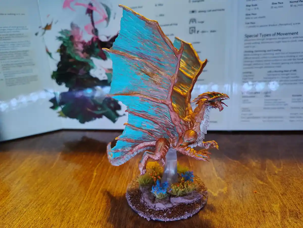 A hand-painted miniature dragon figurine with large, vibrant blue wings and orange-brown body stands on a textured base with…