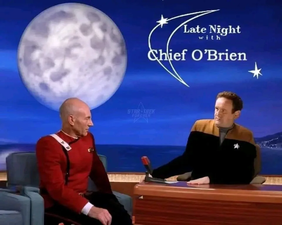 Two men in Star Trek uniforms sit on a talk show set with a large moon in the background. The host, wearing a black and gold…