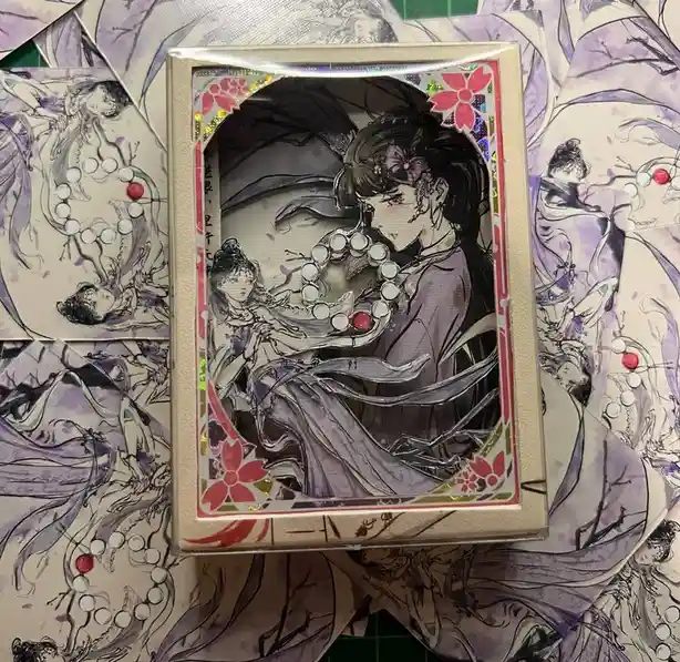 A close-up photo shows a framed anime-style illustration of a woman in flowing purple robes holding a string of white beads…