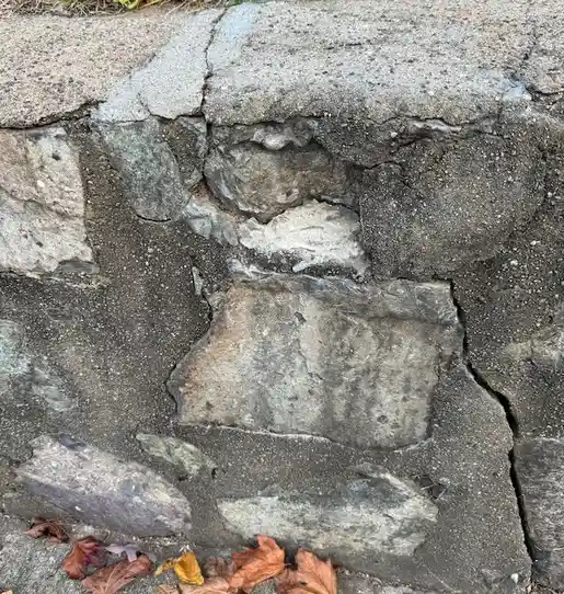 A close-up photo of a cracked, weathered stone wall with visible gaps and loose stones, some autumn leaves scattered at the…