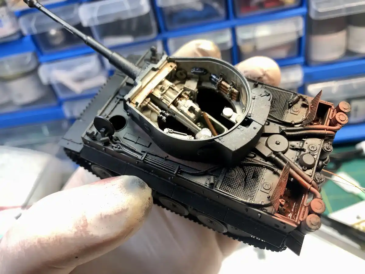 A close-up photo shows a person's hand holding a highly detailed, partially assembled model tank with its turret open…