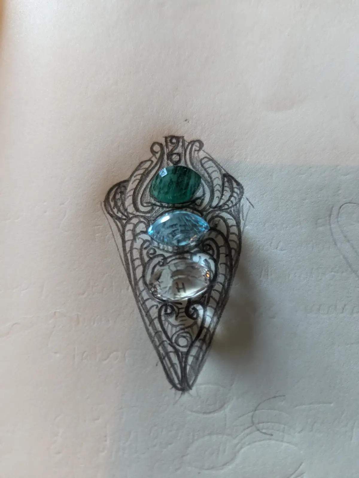 A hand-drawn, ornate, Art Nouveau-style jewelry design sketch on textured paper, featuring three vertically aligned…