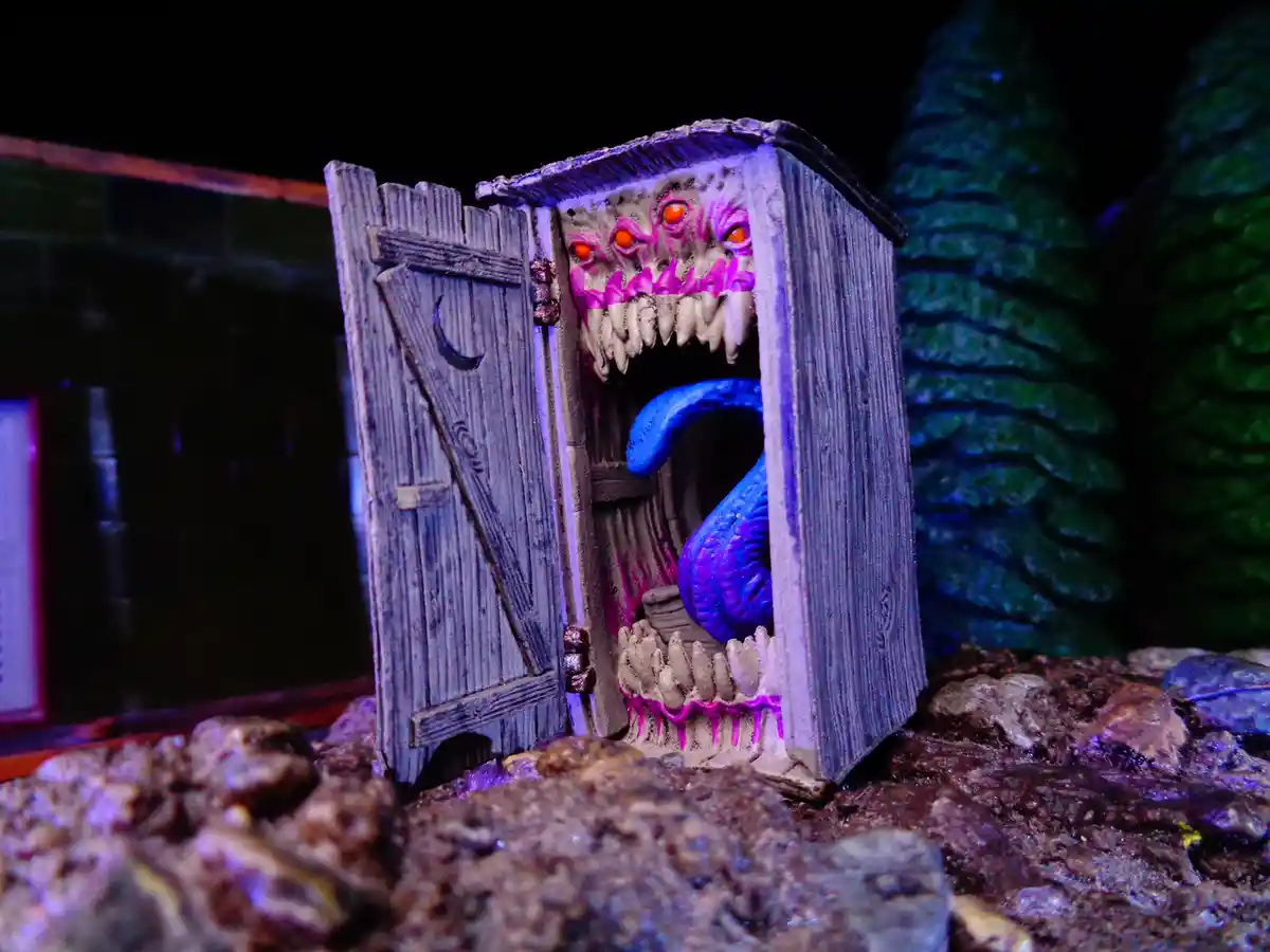 A miniature diorama shows a grotesque, monstrous face with glowing orange eyes and sharp teeth emerging from a wooden…