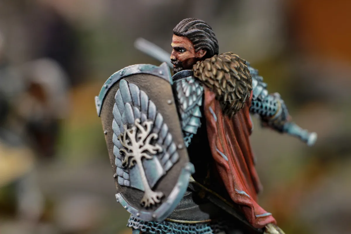 A close-up photo of a detailed fantasy miniature figure of a warrior with a beard, wearing chainmail, a red cloak, and…