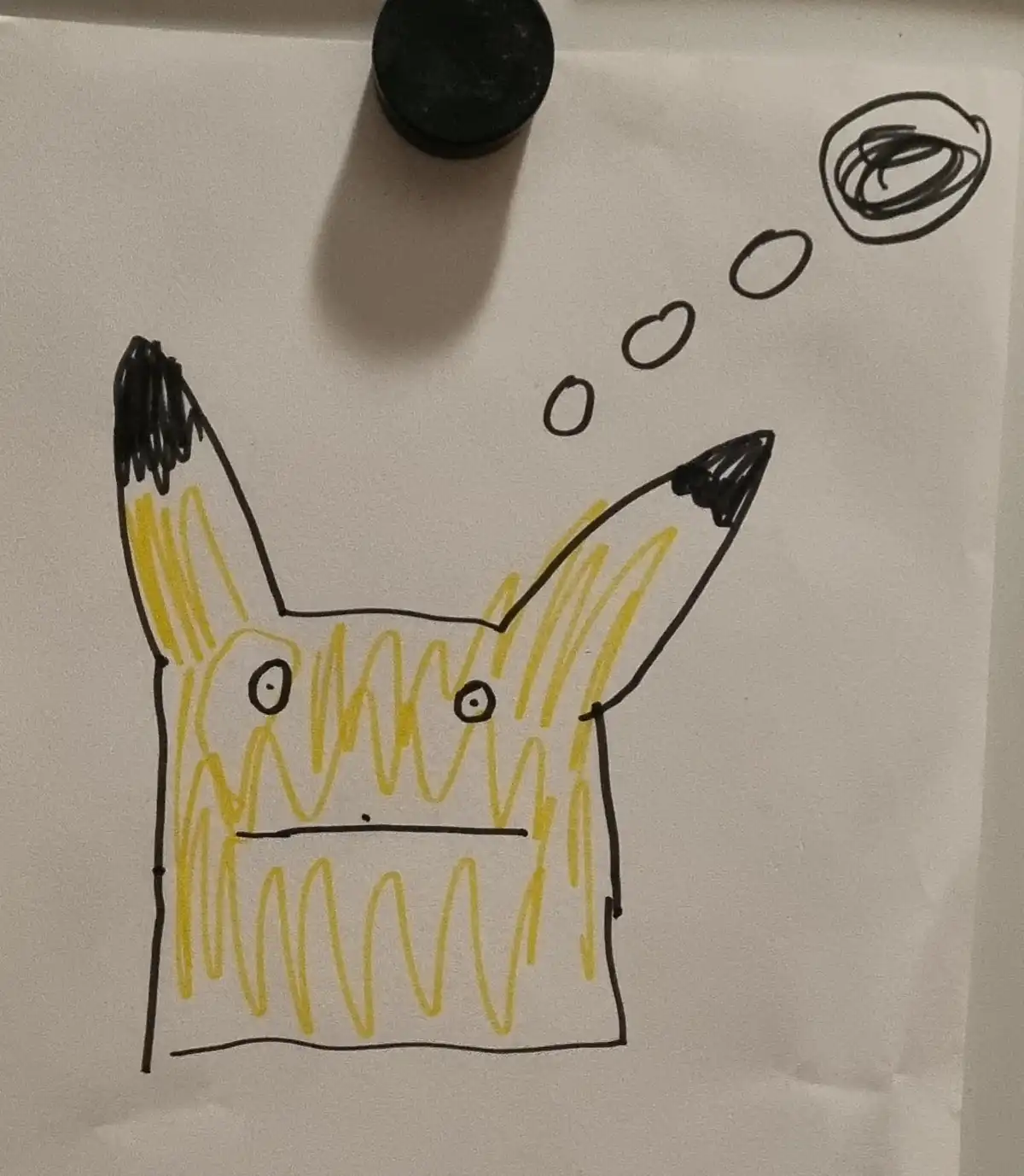 A child's drawing of Pikachu on paper, with yellow scribbles for fur and black-tipped ears, has a thought bubble above its…