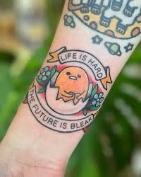 A close-up of a person's forearm showing a colorful tattoo of the character Gudetama, a lazy egg, encircled by the text…