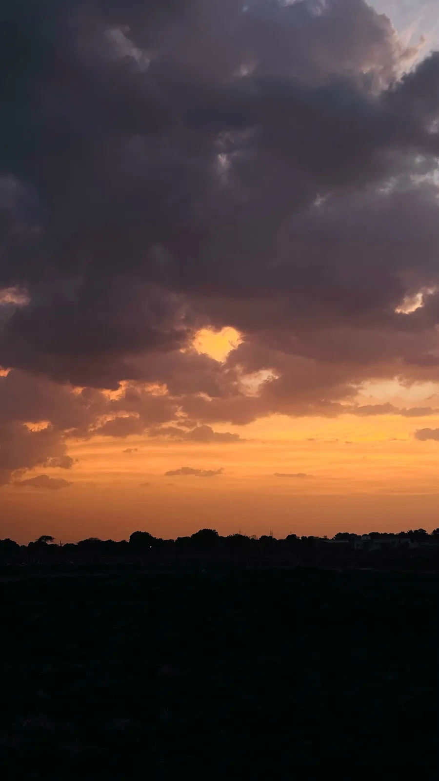 A dramatic sunset photo shows a heart-shaped opening in dark clouds, revealing bright orange sky behind, with a silhouetted…