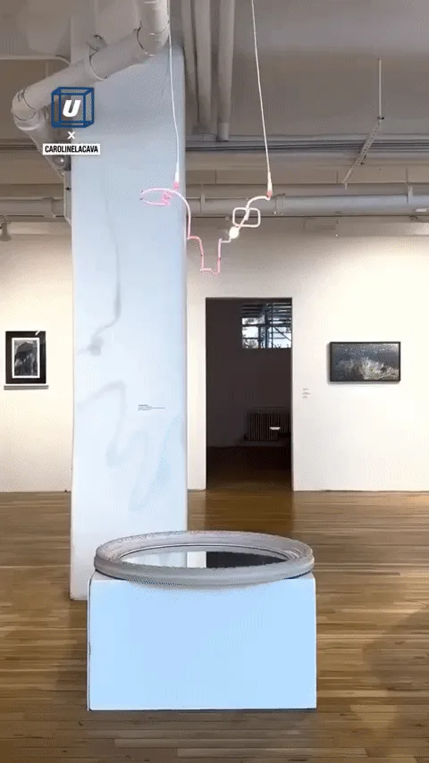 A sequence of images shows a pink neon sculpture of a face hanging above a mirror in an art gallery. The camera pans down to…