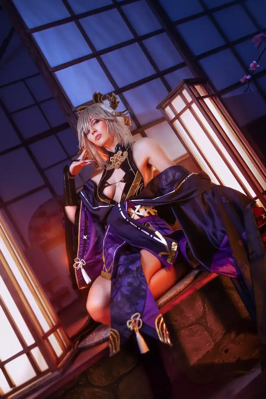 A cosplayer in a detailed purple and black outfit with gold accents and animal ears poses seductively on a wooden bench in a…