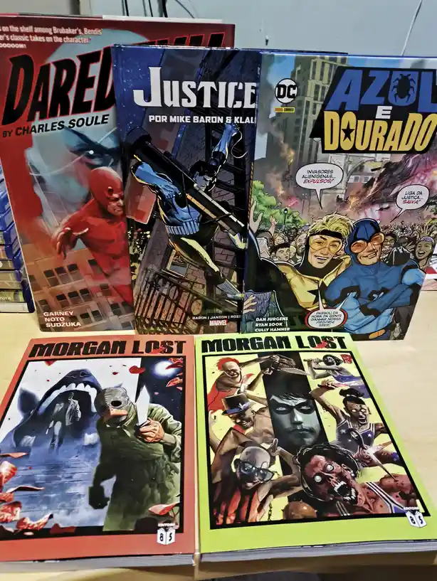 Four comic books are displayed on a wooden surface: 'Daredevil' by Charles Soule, 'Justice' by Mike Baron & Klaas, 'Azul e…