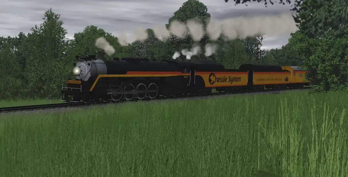 A steam locomotive with 'Chessie System' and 'Chessie Steam Special' branding chugs through a grassy field with trees in the…