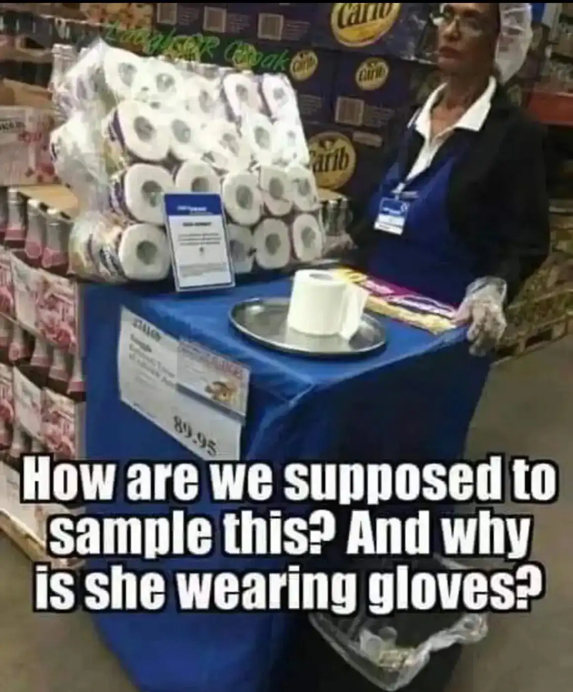 A woman in a store uniform and plastic gloves stands beside a display table covered in a blue cloth. On the table is a…
