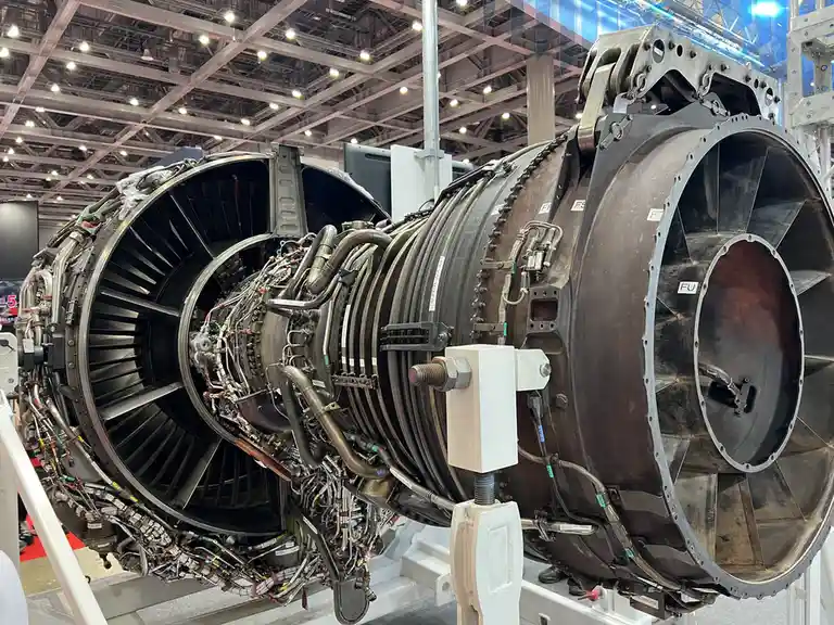 A large, complex jet engine is displayed cut open at an exhibition, revealing intricate internal components like turbines…