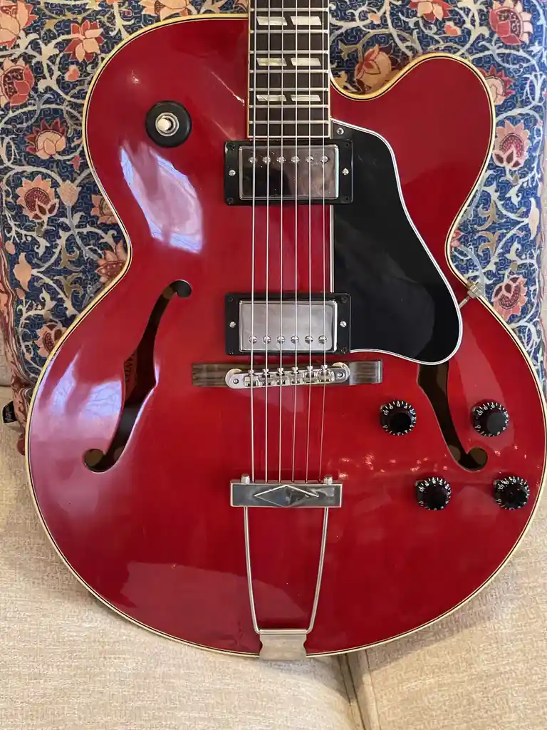 A glossy red semi-hollow body electric guitar with f-holes, two humbucker pickups, and four control knobs rests on a…