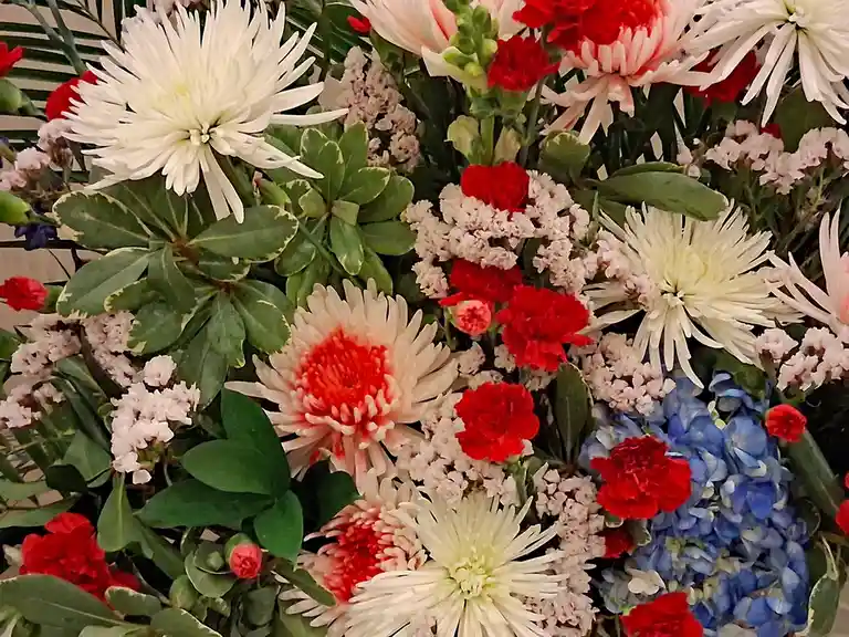 A vibrant floral arrangement featuring white, red, and blue flowers including chrysanthemums, carnations, and hydrangeas…