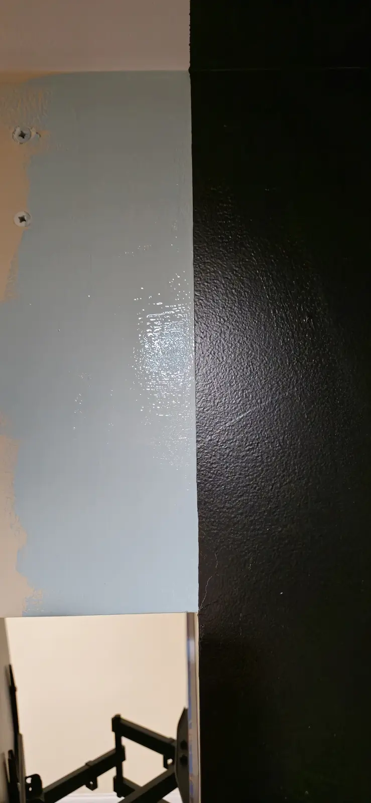 A close-up photo shows a freshly painted light blue wall section next to an adjacent dark textured wall, with visible paint…