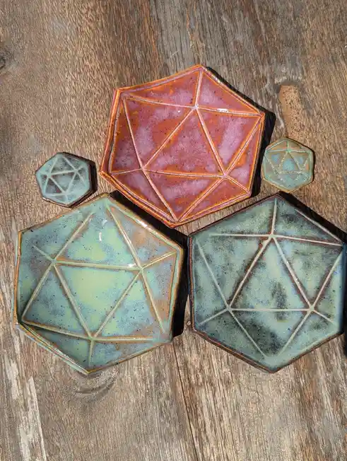 Five ceramic plates shaped like polyhedral dice, commonly used in Dungeons & Dragons, are arranged on a wooden surface. The…