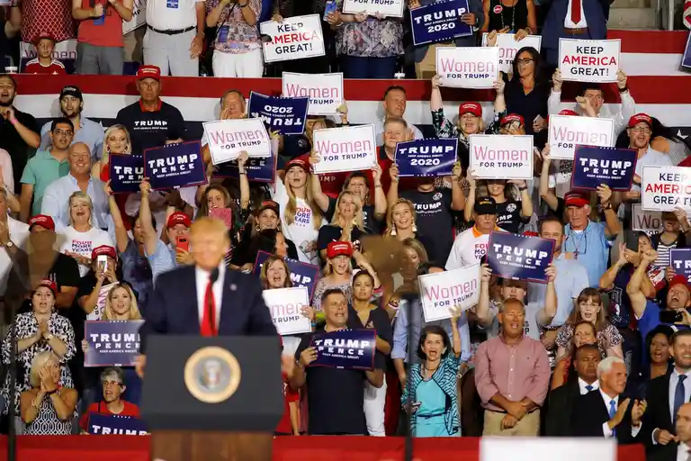 A crowd of enthusiastic supporters at a political rally, many holding signs that say 'Women for Trump' and 'Trump Pence…