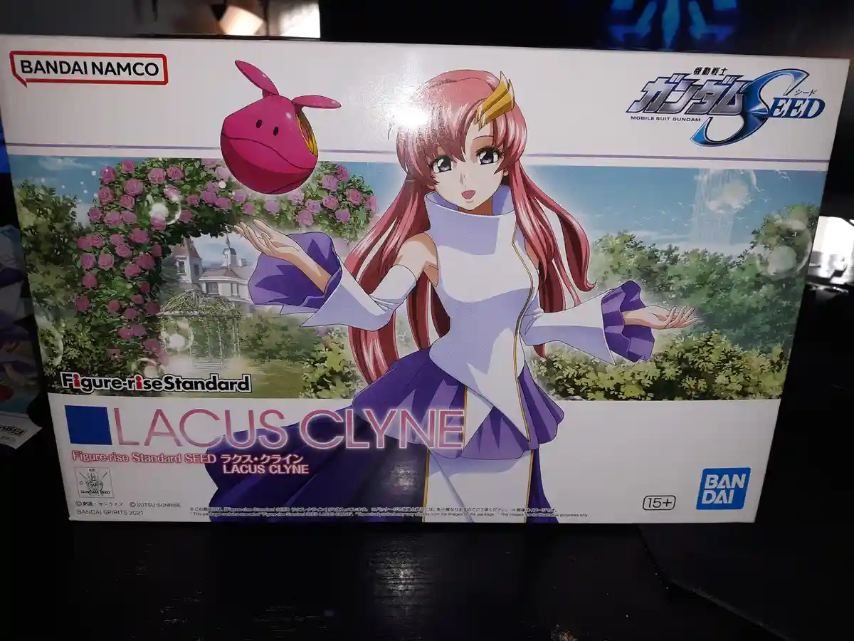 A Bandai Namco Figure-rise Standard model kit box for Lacus Clyne from Mobile Suit Gundam SEED, featuring her in a white and…