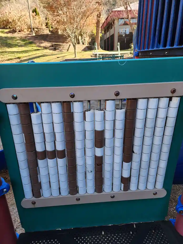 A close-up photo of a playground xylophone with alternating white and brown cylindrical bars, some of which are visibly…
