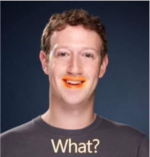 A photo of Mark Zuckerberg with bright orange paint smeared across his mouth and upper lip, looking surprised. He wears a…
