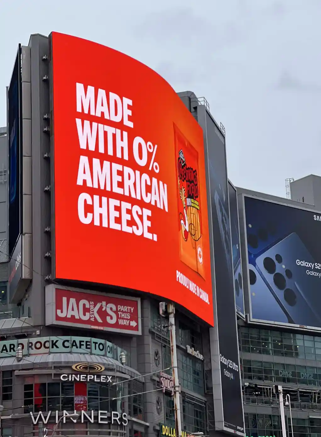 A large red billboard in a city displays an advertisement for Cheez Whiz, stating 'MADE WITH 0% AMERICAN CHEESE.' and…