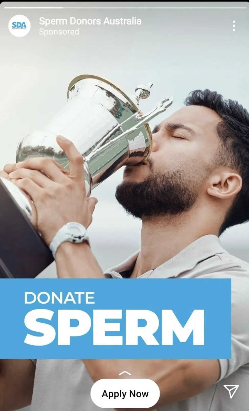 A man with a beard is kissing a large silver trophy, overlaid with a blue banner that says 'DONATE SPERM' and a white 'Apply…
