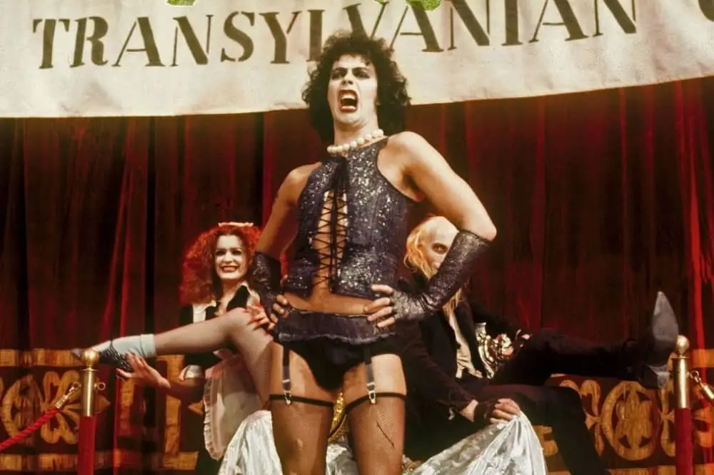 A still from the movie 'The Rocky Horror Picture Show' shows a man in a sparkly corset and suspenders standing center stage…