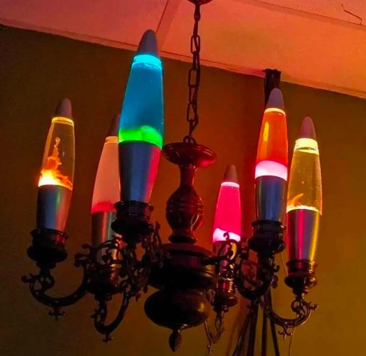 A chandelier with ornate black metal arms and multiple arms ending in lava lamps, each glowing with different colors like…