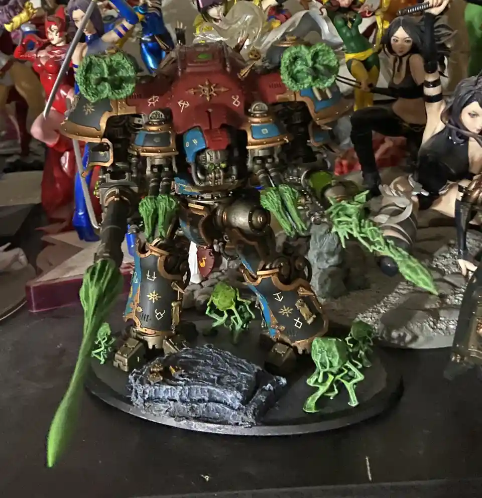 A heavily armored, red-and-blue painted war machine model is covered in bright green, fungus-like growths on its limbs…