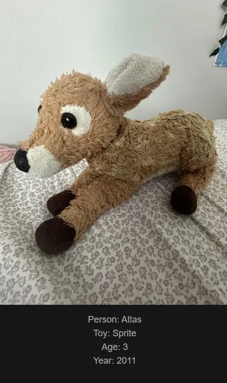 A brown, fluffy stuffed deer toy is lying on a patterned bedspread. Overlaid text at the bottom identifies the toy as…