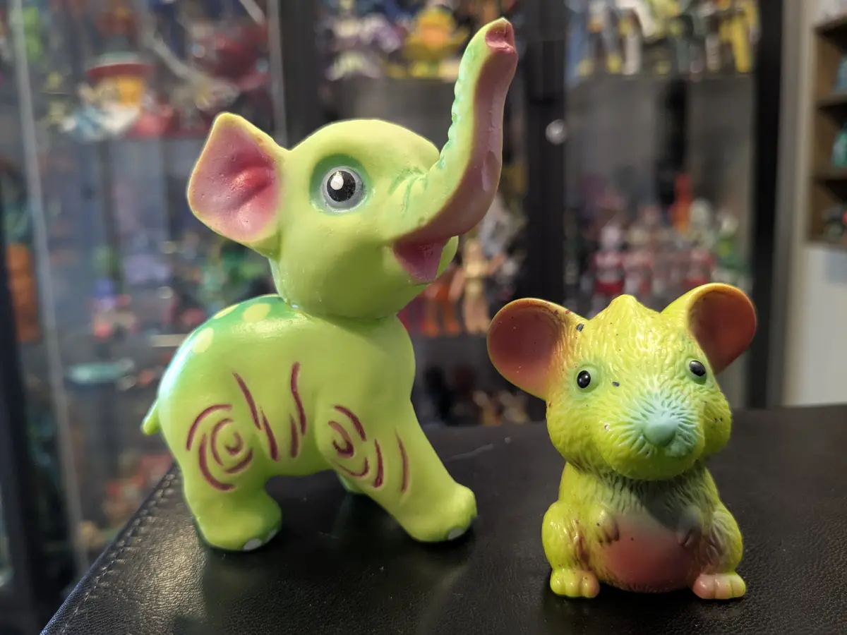 Two brightly colored plastic figurines, one green elephant with raised trunk and red swirl patterns, and one smaller…