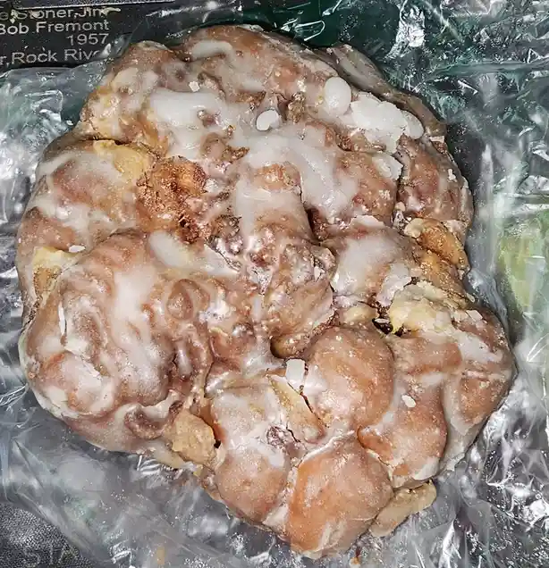 A close-up photo shows a large, irregularly shaped glazed donut with a brain-like texture, sitting in a clear plastic bag…
