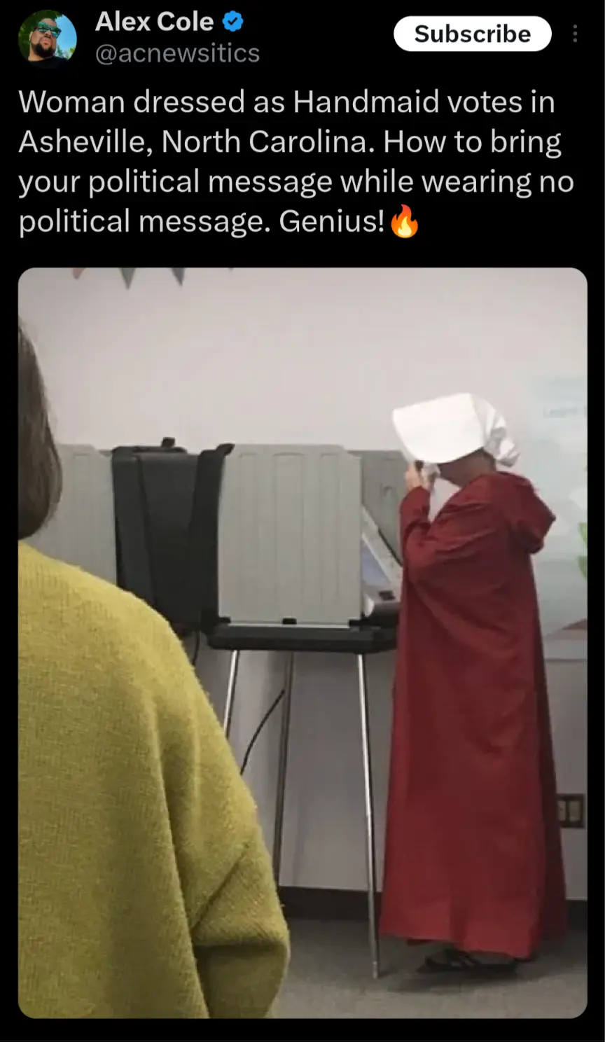 A person wearing a red robe and white bonnet, resembling a Handmaid from 'The Handmaid's Tale,' is standing at a voting…