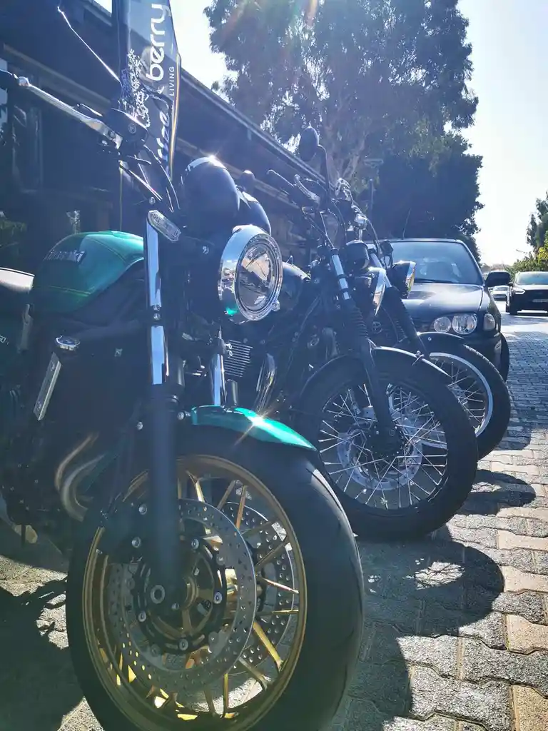 A close-up photo of two motorcycles parked on a cobblestone street under bright sunlight, with a green Suzuki in the…
