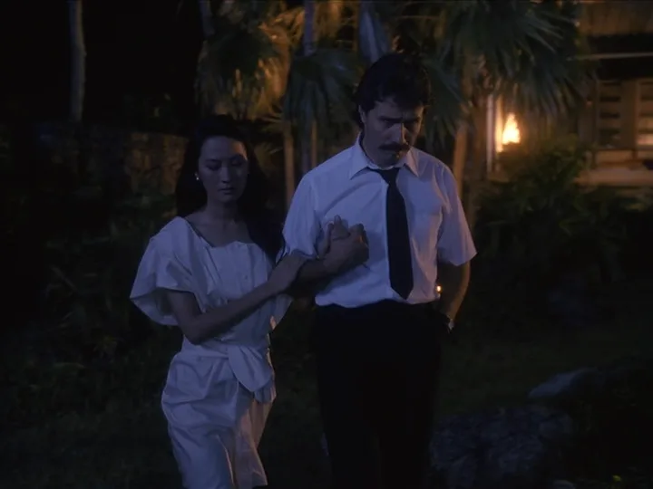 A man in a white shirt and black tie walks slowly at night with a woman in a white dress holding his arm; overlaid text…