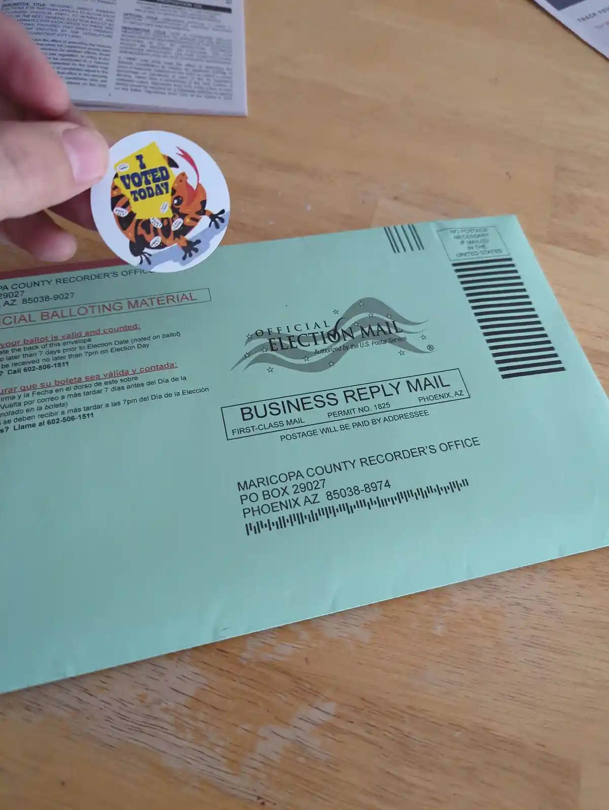A hand holds a circular sticker featuring a cartoon tiger holding a sign that reads 'I VOTED TODAY' above a light green…