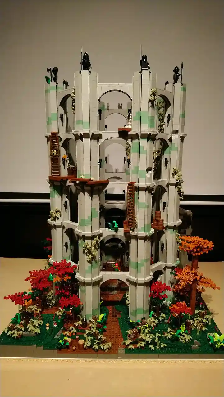 A detailed Lego castle model constructed with white and green bricks, featuring multiple arches, towers, and ladders. Black…