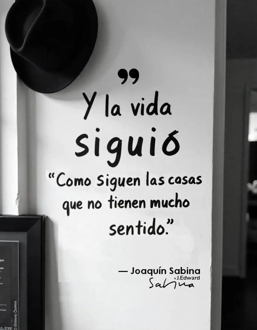 A black-and-white photo shows a white wall with handwritten Spanish text overlaid. A black fedora hat hangs on the wall…