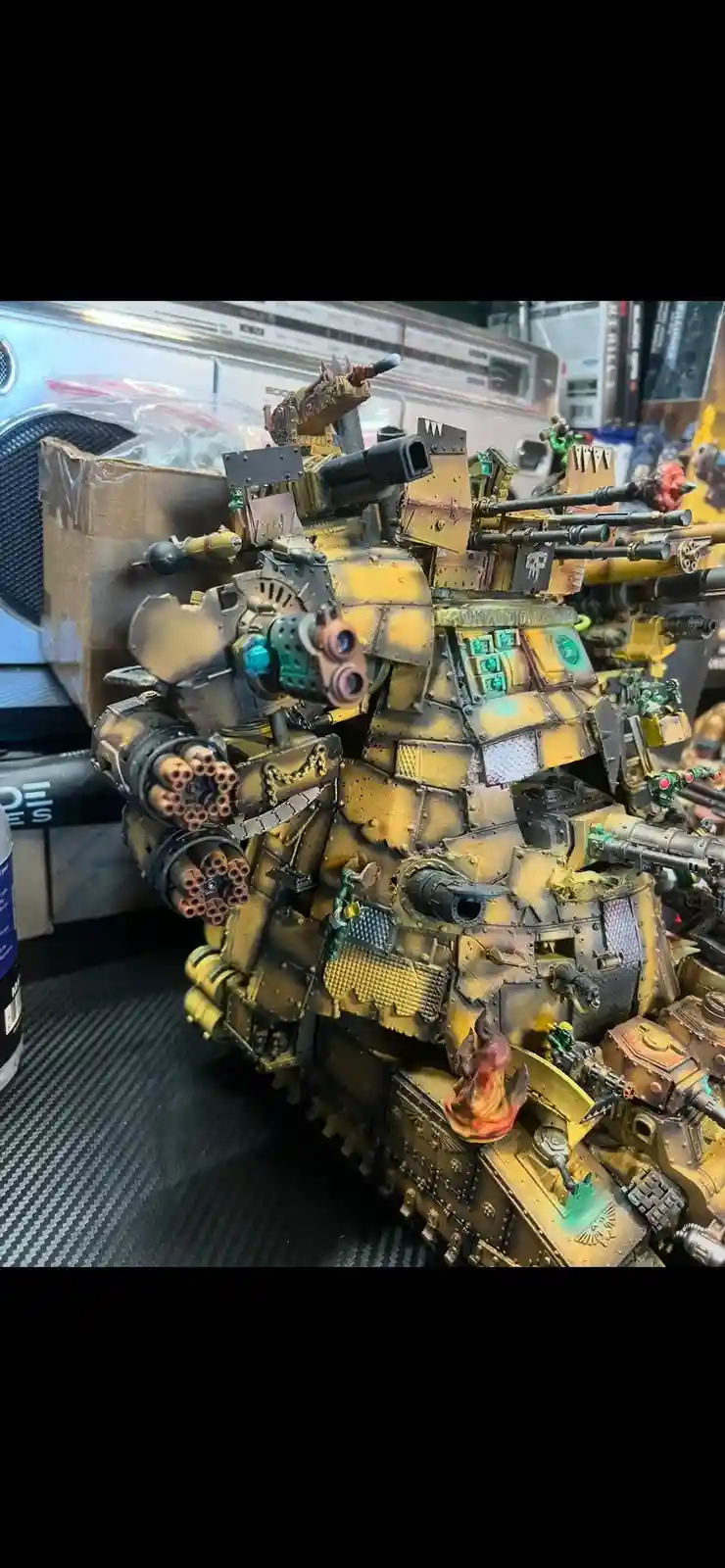 A heavily armed, yellow-painted, custom-built Warhammer 40k tank model with numerous weapons and weathered details sits on a…