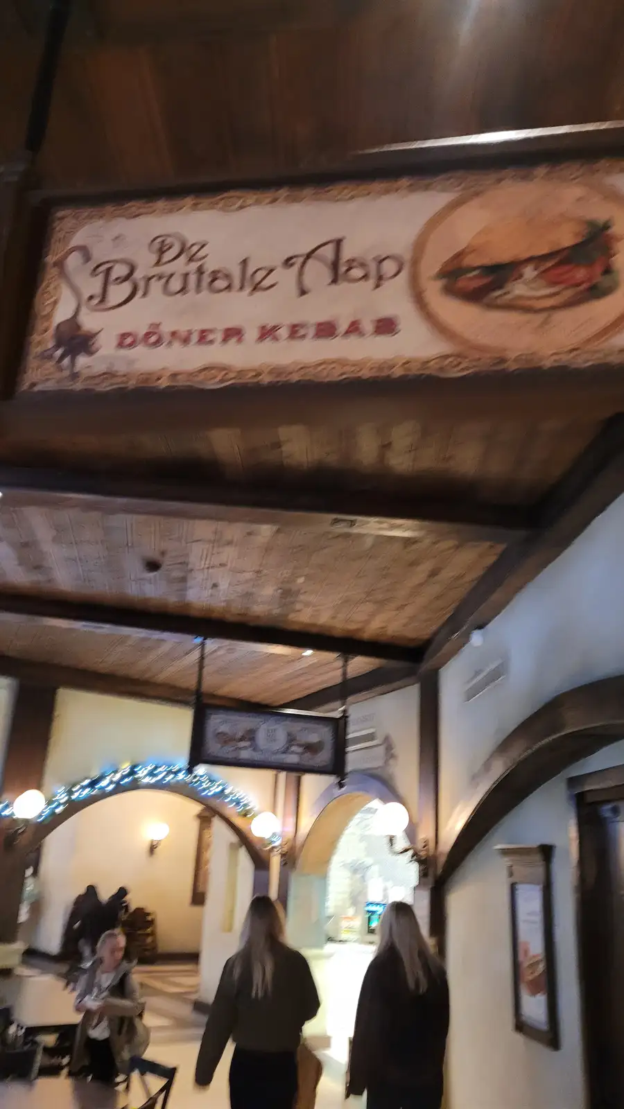 A photo of a restaurant's sign that reads 'Dz Brutalz Nap DÖNER KEBAB' with an image of a sandwich, mounted above a…