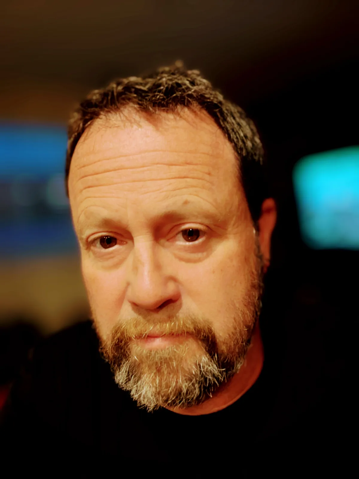 A close-up photo of a middle-aged man with a graying beard and intense, slightly furrowed brow, looking directly at the…