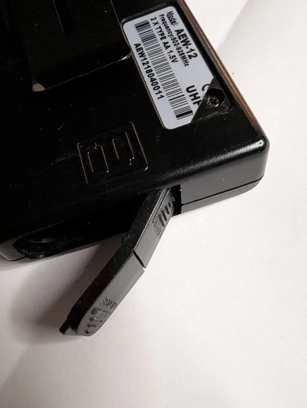 A close-up of a black handheld radio's battery compartment, showing a partially inserted battery and a white label with a…
