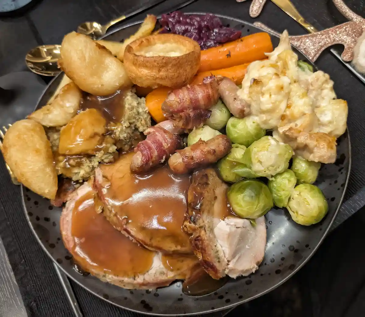 A plate of traditional roast dinner featuring sliced turkey covered in gravy, roasted potatoes, Yorkshire pudding…