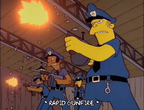 A still image from The Simpsons shows a police officer in a blue uniform firing a weapon with a visible muzzle flash, while…